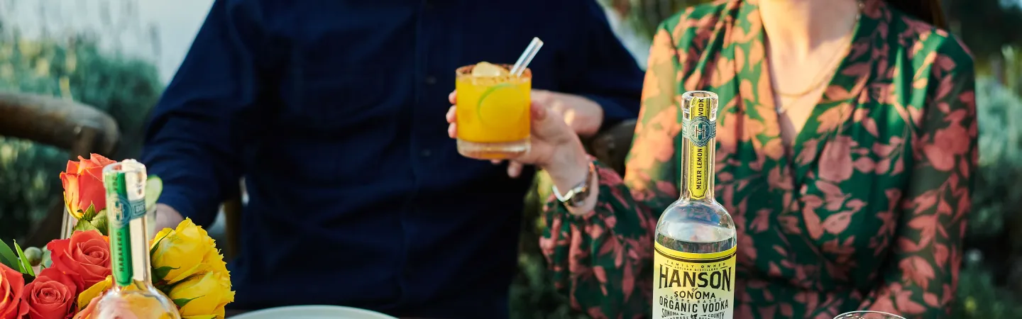 Person holding yellow cocktail with lemon vodka bottle